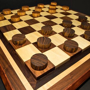 May include: A handcrafted wooden checkers board with alternating light and dark squares. The board is framed with a dark wood border and features matching wooden checkers pieces. The game board is a classic strategy game.