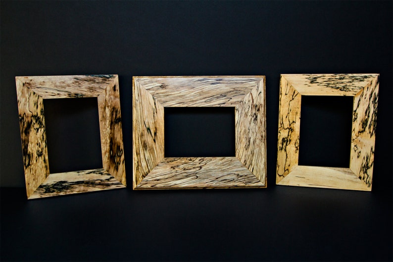 Op de afbeelding: Drie houten fotolijsten met een natuurlijke houten afwerking en zwarte houtnerf accenten. De lijsten zijn in een rij gerangschikt.