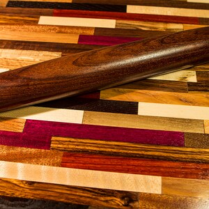 May include: A dark brown wooden rolling pin on a colorful wooden surface. The surface is made of different types of wood, creating a patchwork pattern.