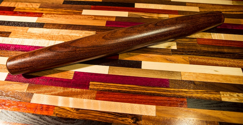 May include: A dark brown wooden rolling pin on a colorful wooden surface. The surface is made of different types of wood, creating a patchwork pattern.