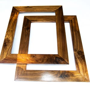 May include: Two wooden picture frames with a rich, dark brown finish. The frames are rectangular with a beveled edge, showcasing the natural wood grain. The frames are overlapping, creating a layered effect, and are set against a white background.