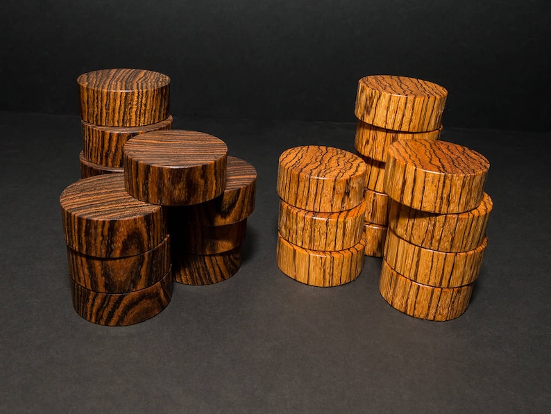 May include: Several stacks of cylindrical wooden pieces with a rich, dark brown and tan striped grain pattern. The pieces are arranged on a dark surface, creating a visually appealing display. The wood's natural grain is prominent.