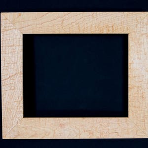 Könnte beinhalten: Ein rechteckiger Bilderrahmen aus hellem Holz mit natürlicher Maserung. Der Rahmen hat ein schlichtes Design mit Gehrungs-Ecken und einem dunklen Hintergrund.