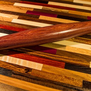 May include: A dark purple wooden rolling pin on a multi-colored wood surface.