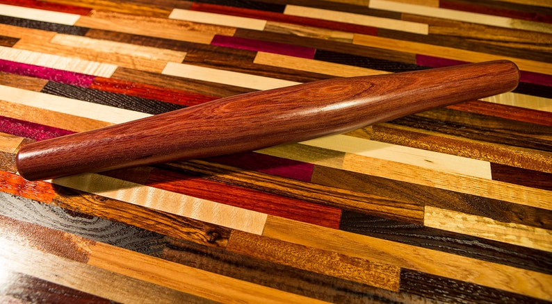 May include: A dark purple wooden rolling pin on a multi-colored wood surface.