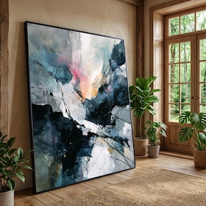 Puede incluir: Gran impresión artística abstracta enmarcada. La obra presenta una mezcla de colores como azul, gris, rosa y blanco, con pinceladas audaces. La pintura se apoya en una pared en una habitación con suelos de madera y grandes ventanas.