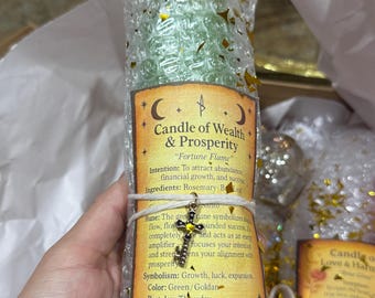 May include: A green candle wrapped in bubble wrap with gold confetti. The candle has a label that reads "Candle of Wealth & Prosperity" with details about its intention, ingredients, and symbolism. A small cross charm is tied to the candle.