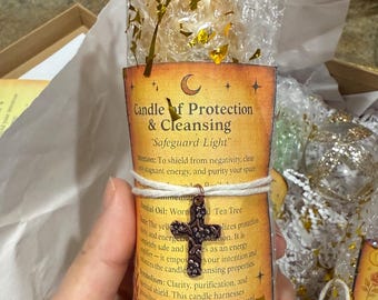 May include: A candle labeled "Candle of Protection & Cleansing" with the text "Safeguard Light." The candle is wrapped in bubble wrap and tied with twine, featuring a decorative cross charm. Gold confetti accents the packaging.