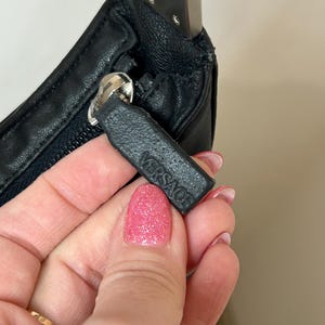 May include: Close-up of a black leather handbag with a silver zipper and chain strap. The zipper pull features the embossed brand name "VERSACE". The bag is held by a person.