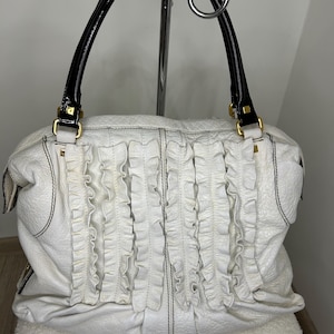 May include: White leather handbag with black stitching and ruffled detailing. Features black patent leather handles with gold-tone hardware. The bag is a soft, slouchy style.
