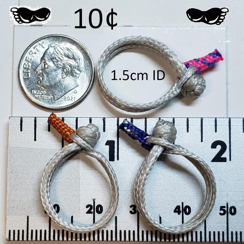 May include: Close-up of three gray rope rings with colorful accents. One ring has a pink and blue accent, another has an orange accent, and the third has a blue accent. The rings are next to a dime and a ruler. The text "1.5cm ID" is visible.