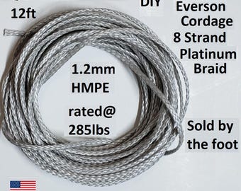 Puede incluir: Una cuerda plateada enrollada, etiquetada como "Everson Cordage 8 Strand Platinum Braid". La cuerda mide 3,66 metros de largo, 1,2 mm HMPE y está clasificada para 129,27 kg. También se ve el texto "Sold by the foot".