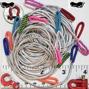 Puede incluir: Una cuerda plateada enrollada con bucles coloridos y acentos rojos, azules, rosas y verdes. La imagen incluye un grillete rojo y una regla para la escala. Los bucles est&aacute;n hechos de cord&oacute;n trenzado.