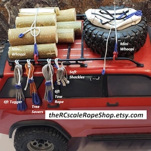 Puede incluir: Un cami&oacute;n de juguete rojo con una llanta negra, cuerdas y troncos de madera en la parte superior. La imagen incluye el texto "Mini Whoopi", "Soft Shackles", "6ft Tugger", "Tree Savers", "6ft Tow Rope" y "theRCscaleRopeShop.etsy.com".