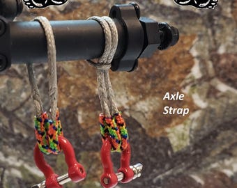 May include: Close-up of two red axle straps with colorful braided accents. The straps are attached to a black metal bar with a silver rope. The text "Axle Strap" is visible, along with a website address.