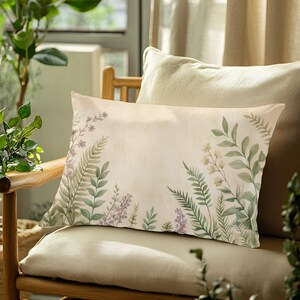 May include: A rectangular pillow with a floral design. The pillow features a cream-colored background with watercolor illustrations of green ferns, lavender, and white flowers. The pillow is placed on a wooden chair with a beige cushion.