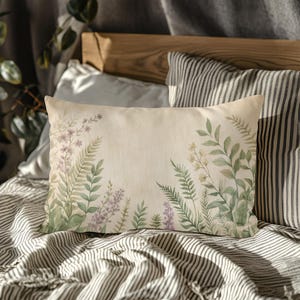 May include: Rectangular decorative pillow with a botanical design. The pillow features a cream-colored background with watercolor illustrations of ferns, lavender, and other greenery in shades of green and purple. The pillow is on a striped bedspread.