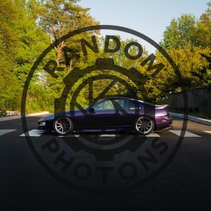 May include: A dark purple sports car is parked on a road with white lines, surrounded by green trees and a clear blue sky. The car has custom wheels and a sleek design. The image has a watermark that says "RANDOM PHOTONS".