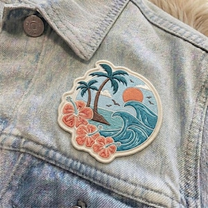 May include: Embroidered patch featuring a tropical beach scene with palm trees, waves, and hibiscus flowers. The patch is in shades of blue, orange, and pink, and is attached to a light blue denim jacket.
