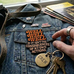 May include: A denim jacket with patches and a keychain. The patches include a lightning bolt, the words "Cult Classic", and a patch that says "WELL WELL WELL IF IT ISN'T THE CONSEQUENCES OF MY OWN ACTIONS". A gold-colored keychain says "CREW".