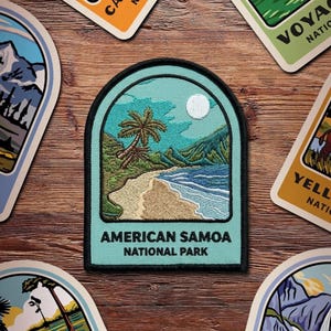 May include: Embroidered patch featuring a beach scene with palm trees, ocean waves, and a full moon. The patch is teal with a black border and the text "AMERICAN SAMOA NATIONAL PARK". Other patches with mountain and nature scenes are visible.