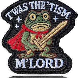 May include: Embroidered patch featuring a green frog wearing a red cape and holding a sword. The patch has the text "T'WAS THE 'TISM M'LORD" in white lettering on a black background. The frog has large, expressive eyes.