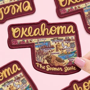 May include: Embroidered patch in the shape of Oklahoma, with the word "Oklahoma" in yellow script. The patch features illustrations of landmarks and the text "The Sooner State."