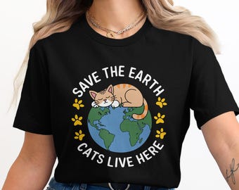 以下が含まれることがあります： 黒いTシャツ。地球儀の上で眠るオレンジ色の猫のグラフィック。テキストは「SAVE THE EARTH, CATS LIVE HERE」で、黄色の足跡が周りにあります。キュートで環境に配慮したデザインです。