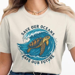 May include: Cream-colored t-shirt featuring a graphic of a sea turtle swimming in a blue wave. The text "SAVE OUR OCEANS SAVE OUR FUTURE" is printed above and below the turtle in a circular design.