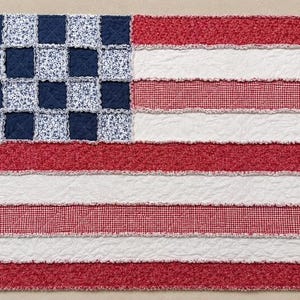 Könnte beinhalten: Eine rechteckige Rag-Quilt-Decke mit Flaggenmotiv. Das Obereck besteht aus abwechselnden marineblauen und blau geblümten Quadraten. Das Feld zeigt horizontale Streifen aus rotem Blumenstoff, weißem Stoff und rot-weiß kariertem Stoff mit ausgefransten Kanten.