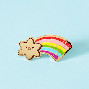 May include: Gold-tone enamel pin featuring a cartoon star with a rainbow shooting out from behind it. The star has a happy face and the rainbow has a red, orange, yellow, green, blue, and purple colour scheme.