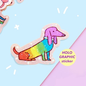 May include: A holographic sticker of a cartoon dachshund dog with a rainbow gradient body and a pink head. The sticker has a glittery effect and the text "HOLO GRAPHIC sticker" is visible.