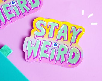 May include: A sticker with a dripping, colorful font that says "Stay Weird" with a single eye in the middle of the word "Weird".