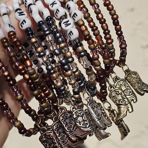 May include: A collection of beaded bracelets featuring white letter beads spelling LIKE ME, interspersed with metallic bronze, copper, and silver-toned seed beads. Each bracelet is finished with a small metal cowboy boot charm pendant.