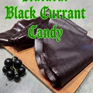 Op de afbeelding: Afbeelding van natuurlijke zwarte bessen snoep. Het donkerpaarse snoep wordt gepresenteerd op een houten snijplank, met een tros zwarte bessen links. De woorden "Natural Black Currant Candy" zijn in groene letters geschreven.