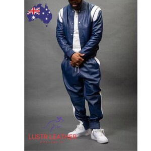 May include: A two-piece navy blue leather tracksuit with white accents. The jacket has white stripes on the shoulders and sleeves. The pants have a white stripe down the side. The outfit is paired with white sneakers.