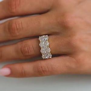 Puede incluir: Primer plano de un anillo con cinco diamantes de talla ovalada engastados en una banda de oro. Los diamantes son claros y brillantes. El anillo se lleva en un dedo.