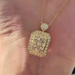 May include: A gold necklace featuring a rectangular, clear gemstone pendant surrounded by smaller, clear gemstones. The pendant is suspended from a delicate gold chain. A smaller, round gemstone is set above the pendant.
