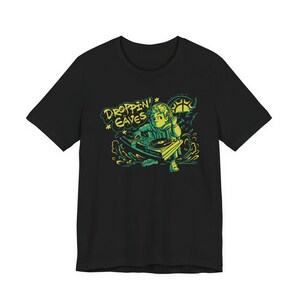 Op de afbeelding: Een zwart T-shirt met korte mouwen en een grafische print van een personage met een koptelefoon achter een DJ-draaitafel. De tekst "DROPPIN' EAVES" staat in het geel boven de figuur, met groene en gele accenten in het ontwerp.