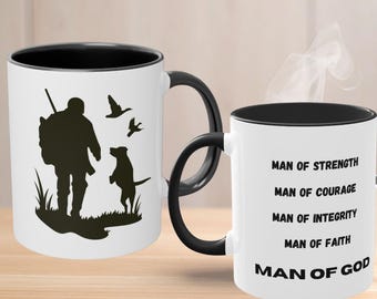 Könnte beinhalten: Zwei weiße Keramikbecher mit schwarzem Innenraum und Henkel. Ein Becher zeigt die schwarze Silhouette eines Jägers mit Hund und fliegenden Vögeln. Der andere Becher trägt den Text: Man of Strength, Man of Courage, Man of Integrity, Man of Faith, Man of God.