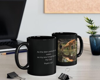 May include: A black ceramic mug featuring a photographic print of a deer drinking from a stream and the white text: As the deer pants for the water, so my soul longs for you My God Psalm 42:1. The mug has a curved handle and a glossy finish.