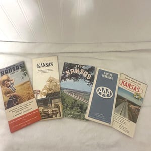 May include: A collection of vintage Kansas travel brochures and maps. The brochures feature images of landscapes, highways, and text. One brochure is from 1962, and another is an AAA map. The color palette includes shades of blue, green, and beige.