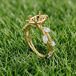 May include: A gold ring setting featuring a central prong mount for a stone, accented by marquise-shaped and round white stones along the band. The band design incorporates leaf-like metal motifs that hold the stones, creating a botanical appearance.