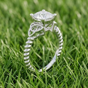 May include: A silver ring with a large, square-cut diamond, set against green grass. The ring has a Celtic knot design and a twisted band. The text "GEMORA DIAM" is visible. The ring is a piece of jewellery.