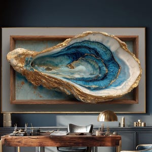 Op de afbeelding: Groot, ingelijst kunstwerk met een gestileerde oesterschelp. De schelp is voornamelijk goud en wit, met blauwe en gouden interieurdetails. Het kunstwerk is gemonteerd op een lichtblauwe achtergrond in een houten lijst. Het stuk wordt tentoongesteld in een goed verlichte kantooromgeving.