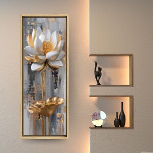 Pode incluir: Uma obra de arte em tela emoldurada com uma flor de lótus 3D com pétalas brancas, detalhes dourados e uma folha de ouro. O fundo tem pinceladas cinza, branco e dourado. A obra de arte é exibida em um ambiente interior moderno.