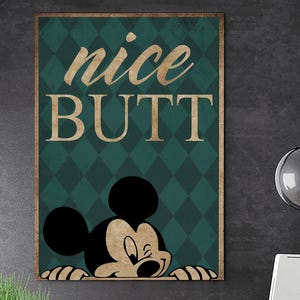 May include: A framed wall art print with the words "nice BUTT" in gold lettering over a teal diamond pattern. A cartoon mouse character peeks from the bottom. The frame has a gold border.