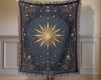 May include: A woven throw blanket featuring a dark blue background with a large, central golden sun face surrounded by radiating rays, stars, and crescent moons. The design includes intricate floral borders and a fringed edge on all sides.