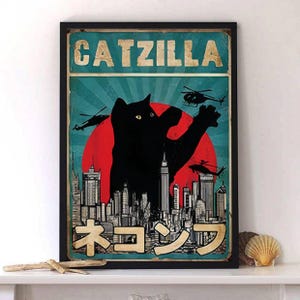 May include: A framed art print featuring a black cat silhouette in a Godzilla-like pose, with the text "CATZILLA" above and Japanese text below. The background includes a red sun, helicopters, and a city skyline.