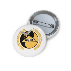 Puede incluir: Botón blanco con un emblema de Tae Kwon Do negro y amarillo que incluye un tigre, un puño y texto coreano. El emblema está enmarcado por una corona de laurel dorada. Tiene un respaldo de alfiler de metal.